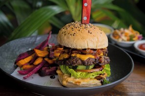A burger with a sesame seed bun, lettuce, cheese, and a beef patty, served on a plate with a side of sweet potato fries.