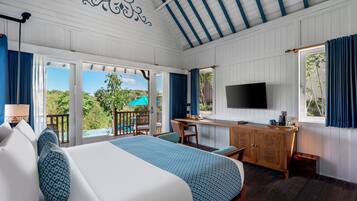 Une chambre d’hôtel équipée d’un lit, d’un bureau, d’une télévision et d’un balcon donnant sur un espace verdoyant.