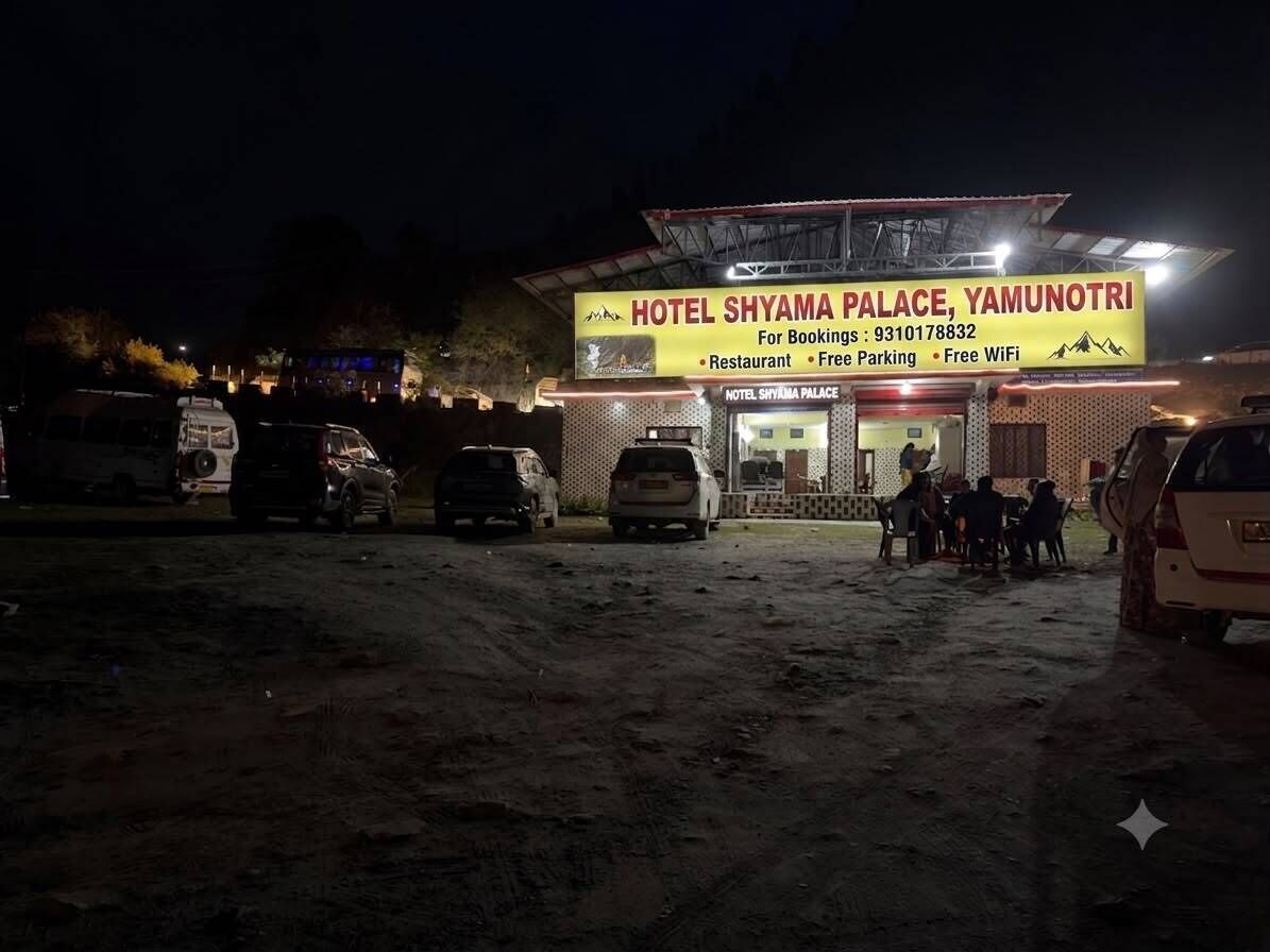 Un hotel con un letrero que indica que es el Hotel Shyama Palace en Yamunotri. Menciona servicios como restaurante, estacionamiento gratuito y WiFi gratuito.