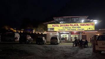 Un hotel con un letrero que indica que es el Hotel Shyama Palace en Yamunotri. Menciona servicios como restaurante, estacionamiento gratuito y WiFi gratuito.