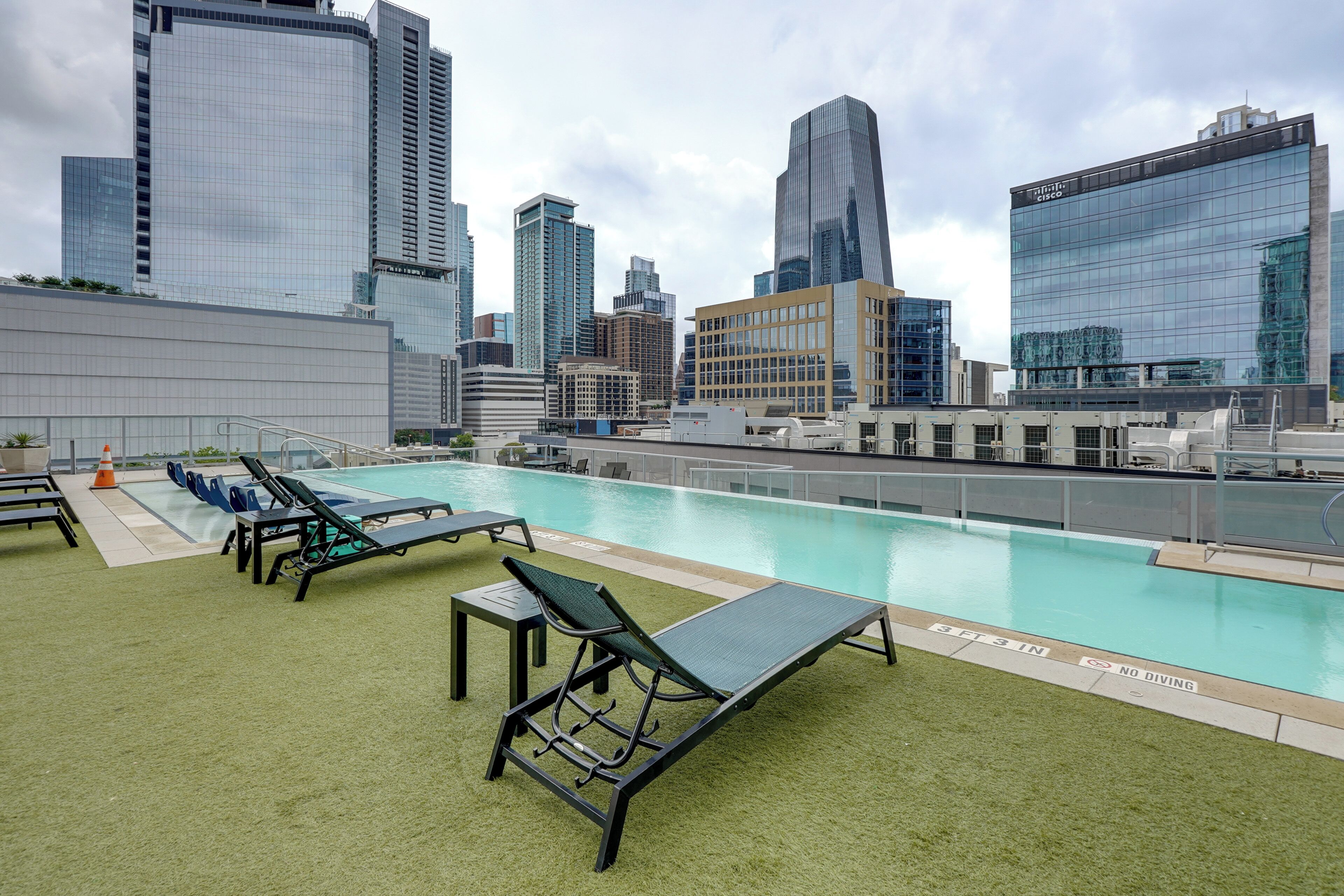 Une piscine sur le toit, avec des chaises longues et une vue panoramique sur la ville en arrière-plan.