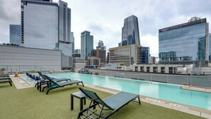 Piscina en la azotea con sillones de descanso y un horizonte urbano al fondo.