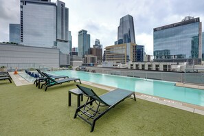Ein Pool auf dem Dach mit Liegestühlen und einer Stadtkulisse im Hintergrund.