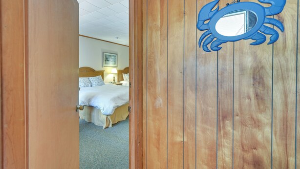 A wooden door with a blue crab decoration, leading to a bedroom with a bed and a nightstand. - Lake Champlain Studio: Fish, Play & Relax (Willsboro)