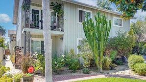Un edificio residencial de dos pisos con un balcón, un cactus y diversas plantas.
