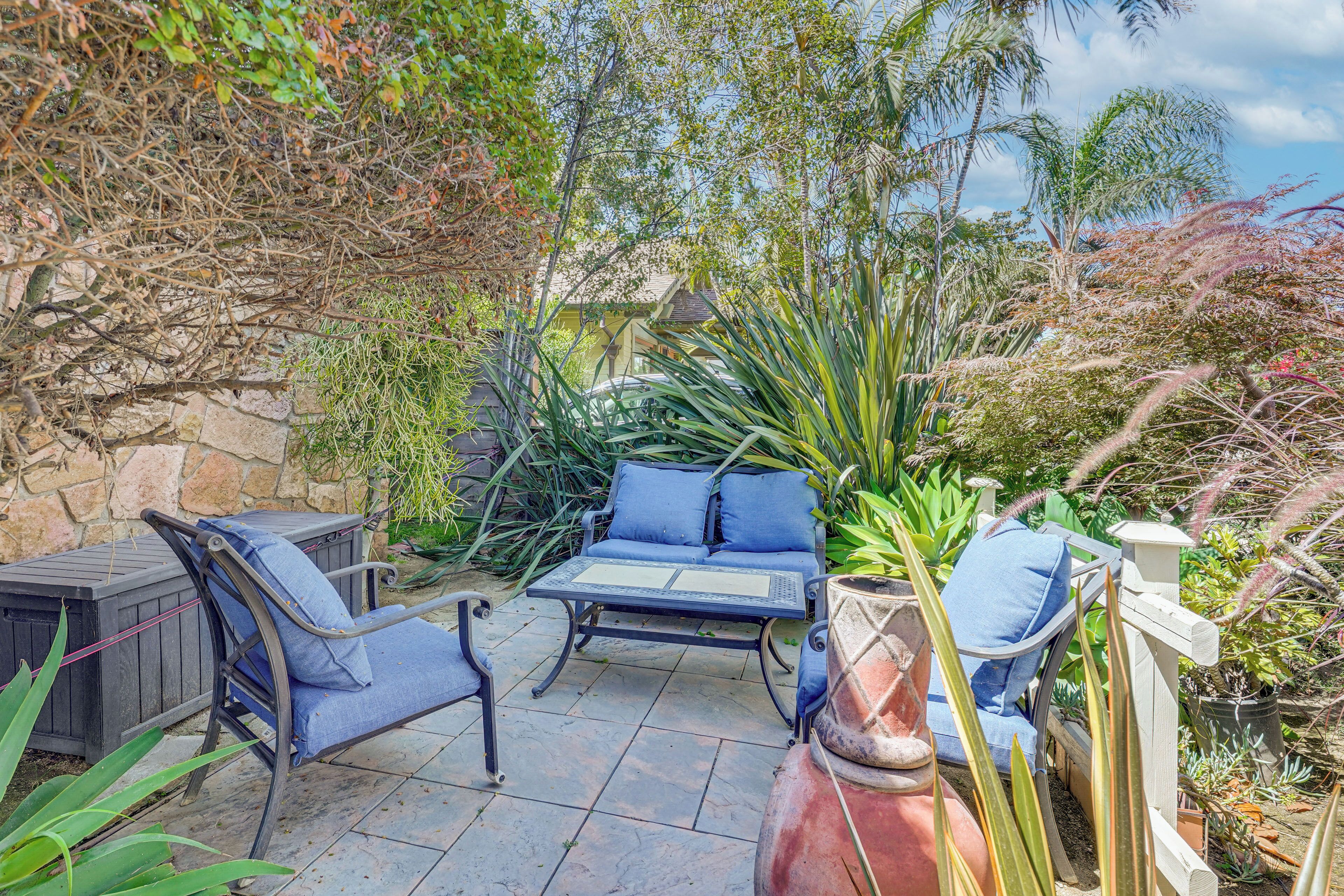 Un espace extérieur aménagé en terrasse, avec deux chaises et une table, entouré de différentes plantes et d’un mur en pierre.
