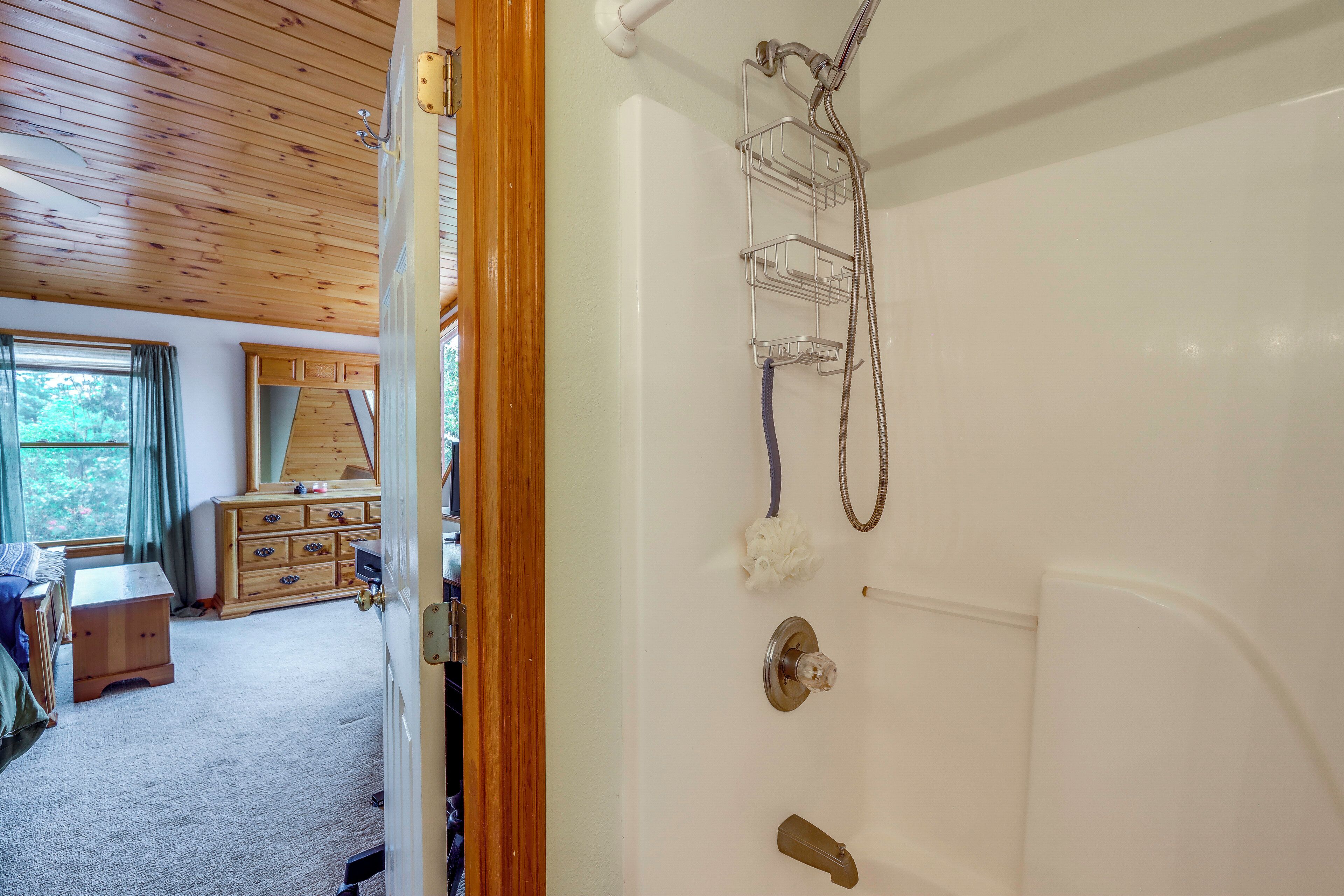 Un baño con ducha, un mueble de madera y vistas a una habitación con cómoda y ventana.