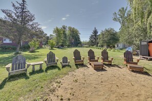 A row of Adirondack chairs and a bench in a grassy outdoor area with trees and a house in the background. - Lake Champlain Escape at Willsboro Inn w/ Dock (Willsboro)