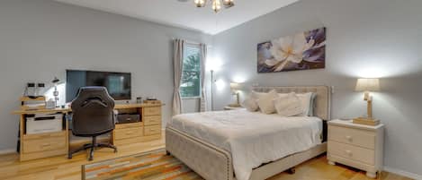Un dormitorio con cama, mesitas de noche, un escritorio con silla, ventilador de techo y una ventana con cortinas.