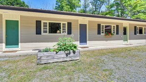 A row of single-story cabins with individual doors and windows, a gravel driveway, and a wooden planter with greenery in the foreground. - Gather Lakeside at Willsboro Inn on Lake Champlain (Willsboro)