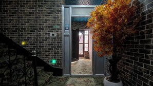 A brick-walled hallway with a door marked 'RECEPTION HERE' and a potted plant with autumn leaves. - Collection O Brein Nishat (Srinagar)