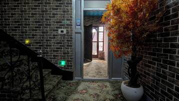 A brick-walled hallway with a door marked 'RECEPTION HERE' and a potted plant with autumn leaves.
