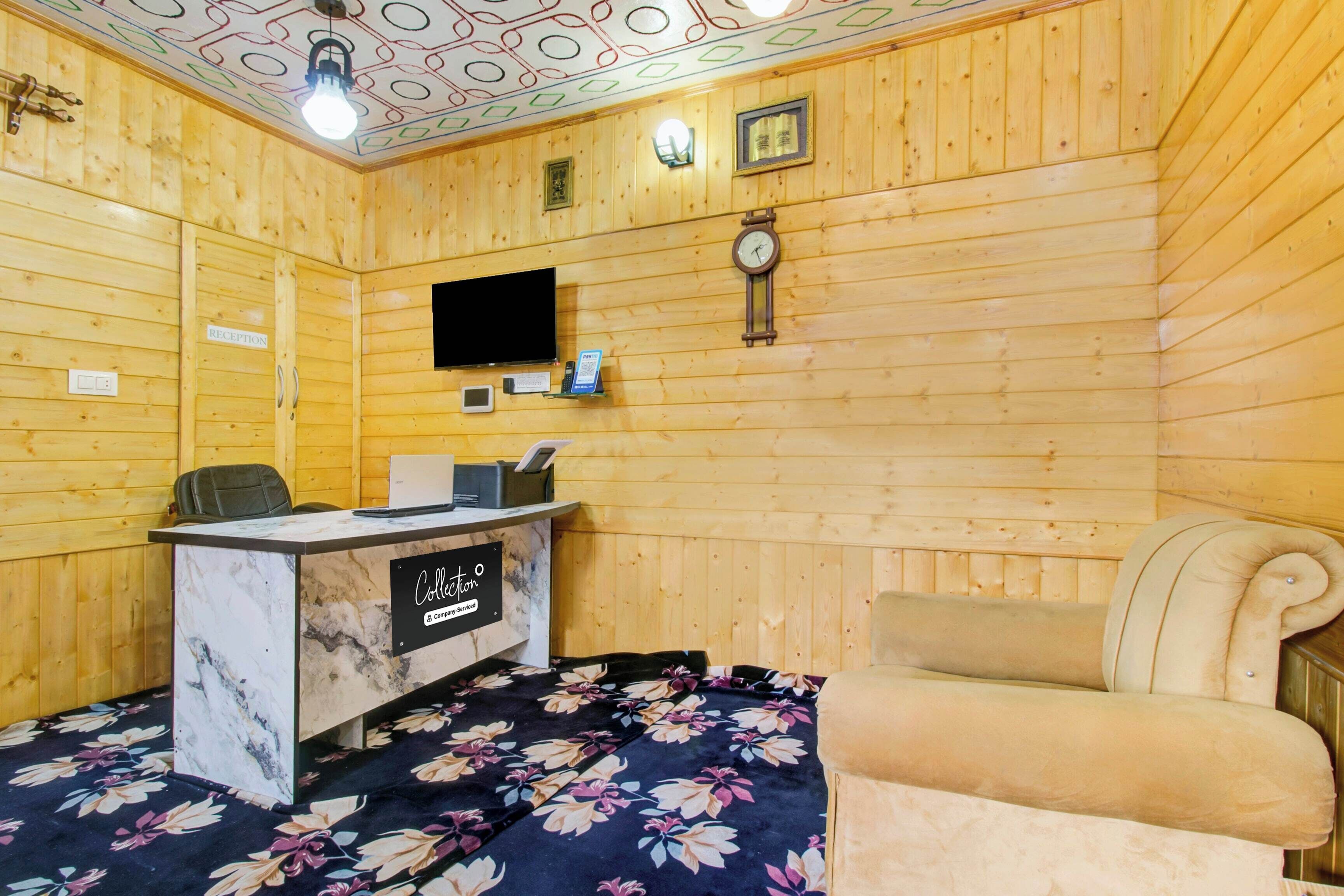 Uma área de recepção com balcão, relógio, televisão e cama com colcha florida.