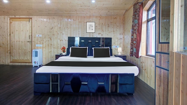A hotel room with a large bed, a bedside table, a heater, and a window with curtains. - Collection O Brein Nishat (Srinagar)