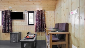 A wooden cabin interior with a television, a table with a tray of cups and a coffee pot, two chairs, and a cabinet. - Collection O Brein Nishat (Srinagar)