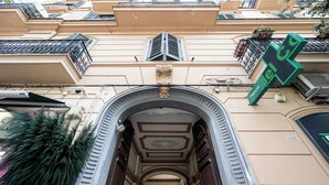 Un ingresso ad arco con soffitto decorativo, un cartello digitale verde e una facciata con balconi e un'antenna parabolica.