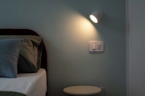 Een kamer met een bed, nachtkastje en een wandlamp.