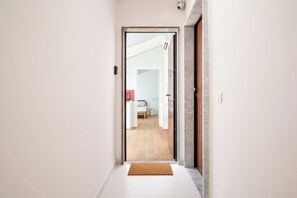 Een hal met een deurmat, een deur die leidt naar een kamer met een bed en een rode kast, en een beveiligingscamera aan de muur.
