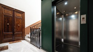 Una porta di legno con maniglia in ottone, una scala in metallo con ringhiera nera e un ascensore verde con interni metallici.