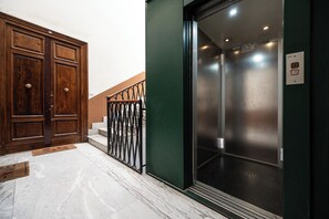 Eine Holztür mit Messingklinke, eine Metalltreppe mit schwarzer Geländer und ein Aufzug mit metallischem Innenraum.