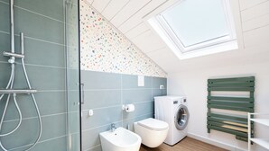 Un bagno moderno con box doccia in vetro, un WC, un bidet, una lavatrice e un lucernario.