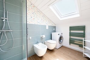 Ein modernes Badezimmer mit Duschkabine aus Glas, Toilette, Bidet, Waschmaschine und Dachfenster.