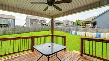 Un patio techado con una mesa y sillas, una valla de madera y casas al fondo.