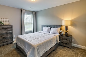 A bedroom with a bed, nightstands, a lamp, a dresser, and a window with curtains. - Porch & Yard! Family Home in Clarksville (Clarksville)
