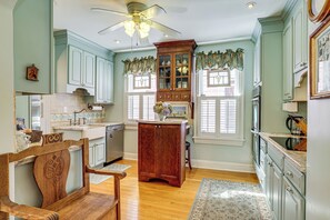 A kitchen with wooden cabinets, a ceiling fan, and a dining area with a wooden chair. - Walkable Victorian Cottage in Historic Ocean Grove (Ocean Grove)