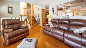 A spacious living room with leather sofas, a wooden staircase, and a kitchen area in the background. - Grill & Fenced Yard! Longmont Home, Walk to Parks (Longmont)