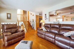 A spacious living room with leather sofas, a wooden staircase, and a kitchen area in the background. - Grill & Fenced Yard! Longmont Home, Walk to Parks (Longmont)