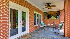 Eine überdachte Terrasse mit Backsteinmauern, einem Deckenventilator und Gartenmöbeln.