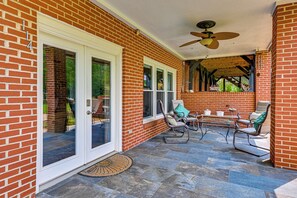 Eine überdachte Terrasse mit Backsteinmauern, einem Deckenventilator und Gartenmöbeln.