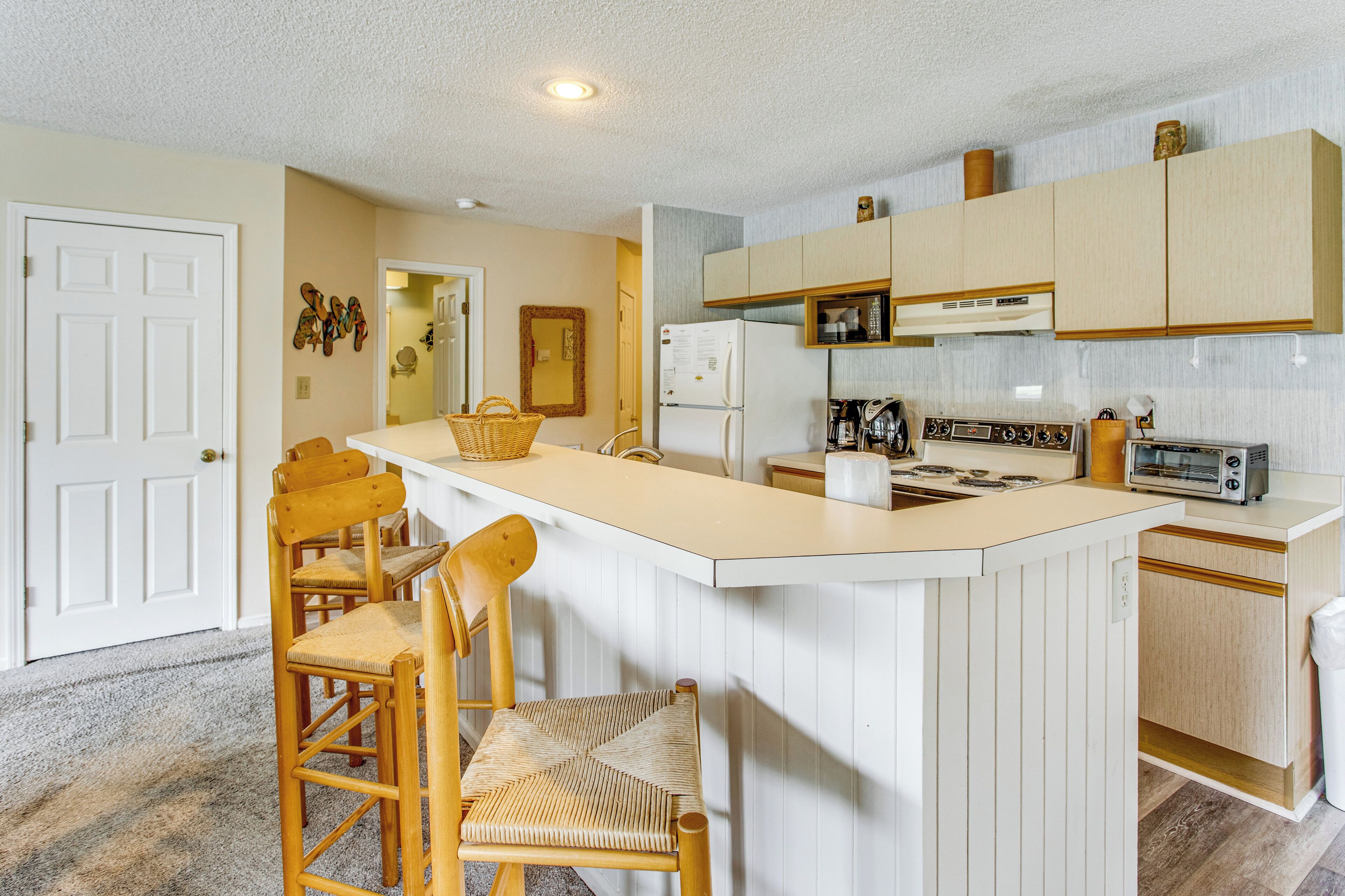 Una cocina con una isla central, sillas de madera, un refrigerador, un microondas, una estufa y un tostador.