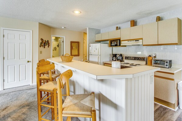 A kitchen with a central island, wooden chairs, a refrigerator, a microwave, a stove, and a toaster. - Near Golf! Waterfront Unit w/ Pool in Sunset Beach (Sunset Beach)