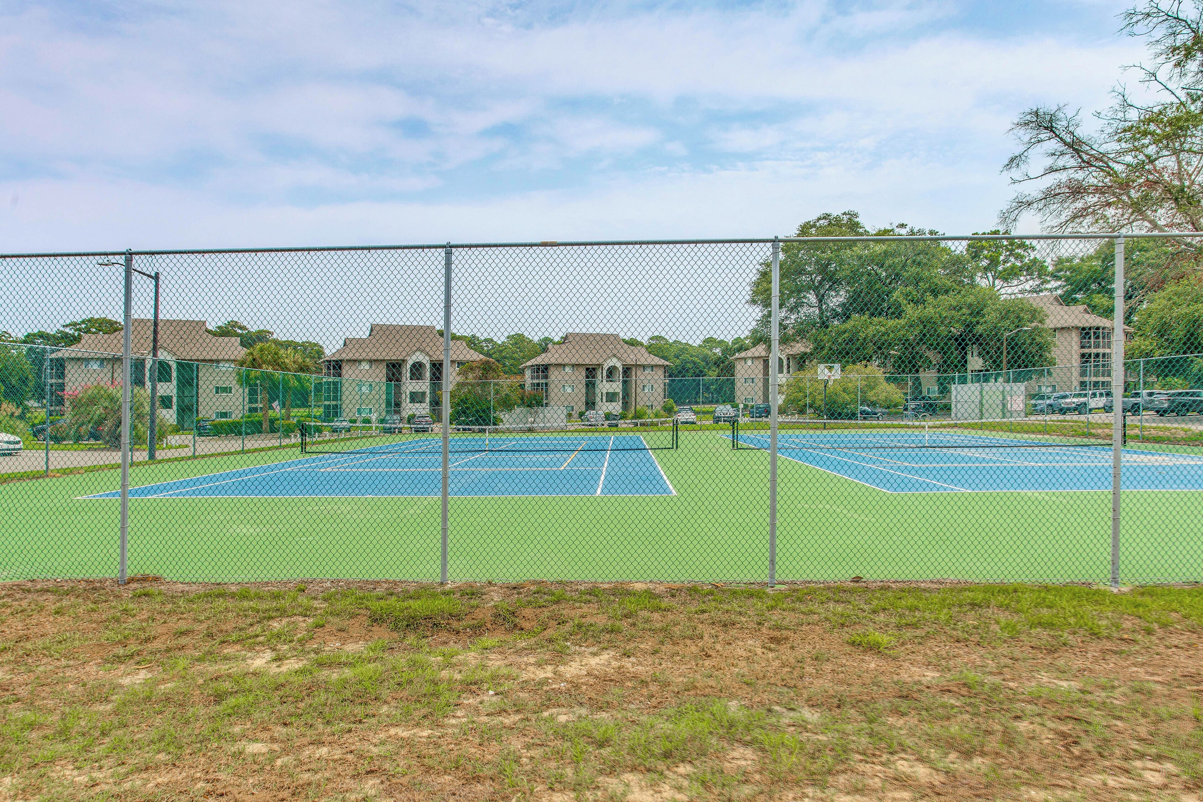 A fenced tennis court with a green surface, surrounded by a chain-link fence.
