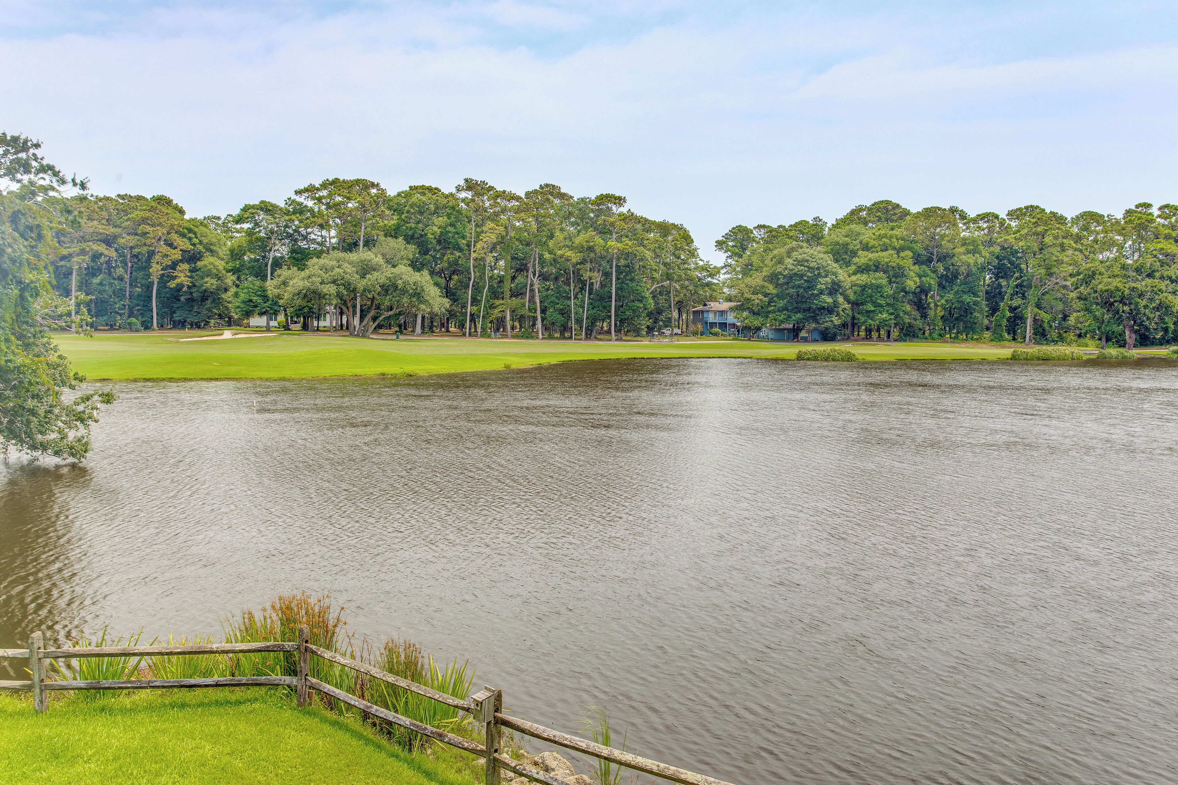 A golf course with a pond, surrounded by trees and a house.