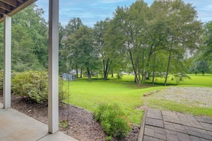 A covered outdoor area with a paved walkway, a grassy lawn, and a view of a residential property with trees and a house.