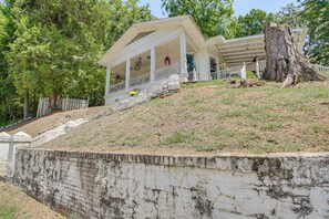 A two-story house with a porch, a large tree in front, and a retaining wall. - Walk to Bathhouse Row! Historic Gem w/ Yard (Hot Springs)