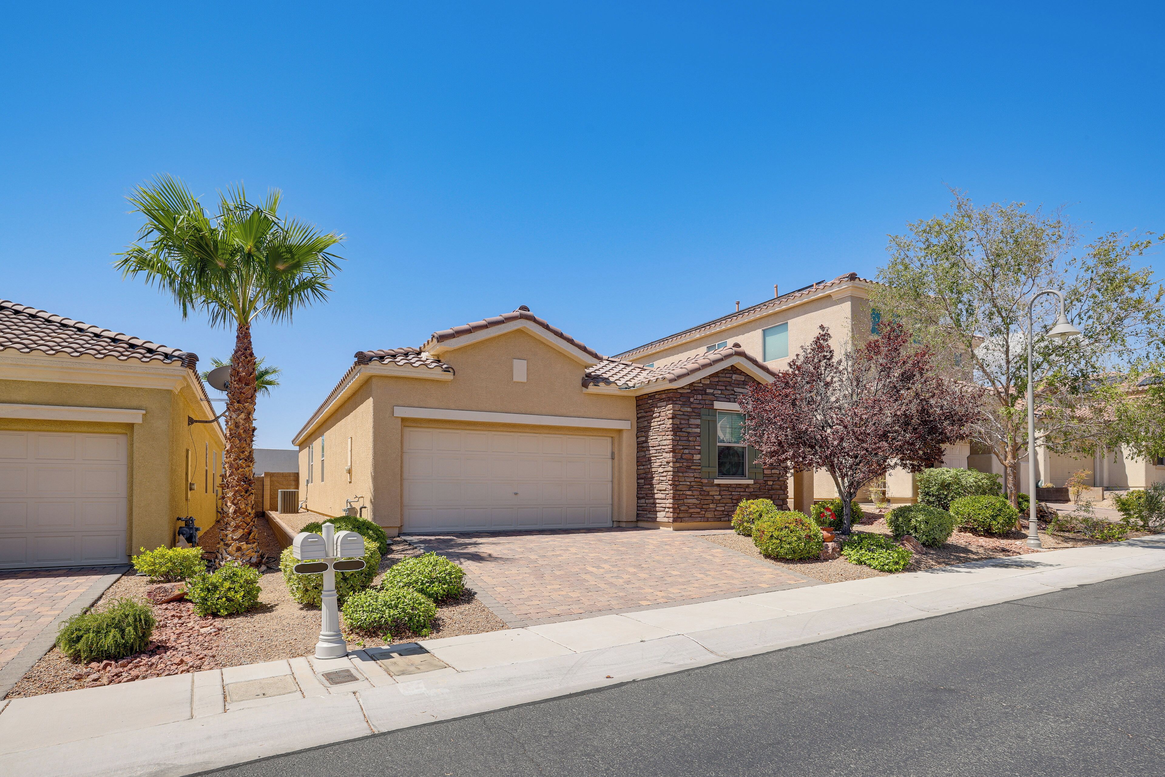 A residential street with houses featuring garage doors, a palm tree, and a well-maintained lawn.