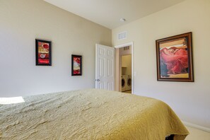 Ein Schlafzimmer mit einem Bett, zwei gerahmten Kunstwerken, einer zur Waschküche führenden Tür und einem Deckenrauchmelder.