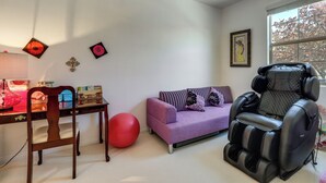 A room with a massage chair, a purple sofa, a red exercise ball, a wooden chair, and a small table with items on it. - Vegas Extended Retreat w/ Furnished Patio (Las Vegas)