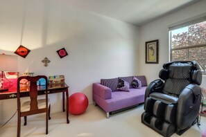 Ein Zimmer mit Massagegerät, einem violetten Sofa, einem roten Gymnastikball, einem Holzstuhl und einem kleinen Tisch mit Gegenständen darauf.