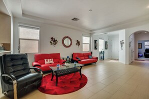Un salón amplio con dos sofás rojos, un sillón de cuero negro, una mesa de centro de vidrio y una alfombra roja.