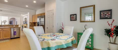 Un comedor con una mesa dispuesta para cuatro personas, sillas blancas, una mesita auxiliar verde y una planta en maceta.