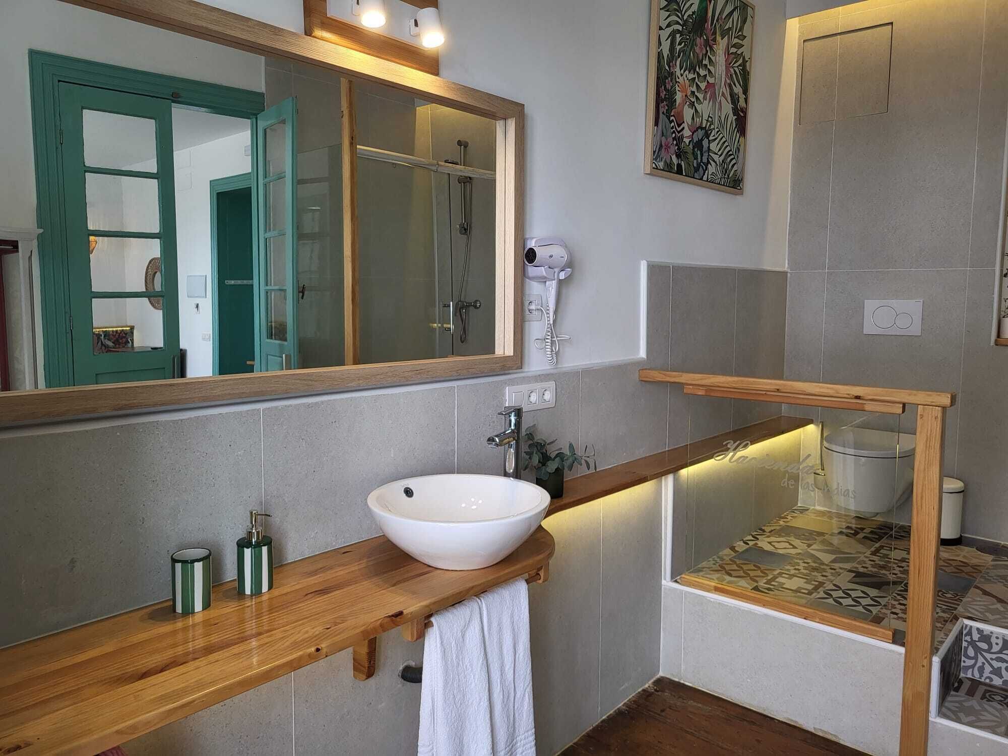 A bathroom with a wooden vanity, a white sink, a mirror, a shower, and a towel rack.
