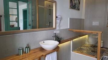 A bathroom with a wooden vanity, a white sink, a mirror, a shower, and a towel rack.