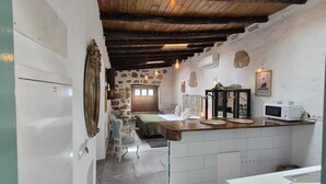 A rustic kitchen with a stone wall, wooden beams, and a white refrigerator.