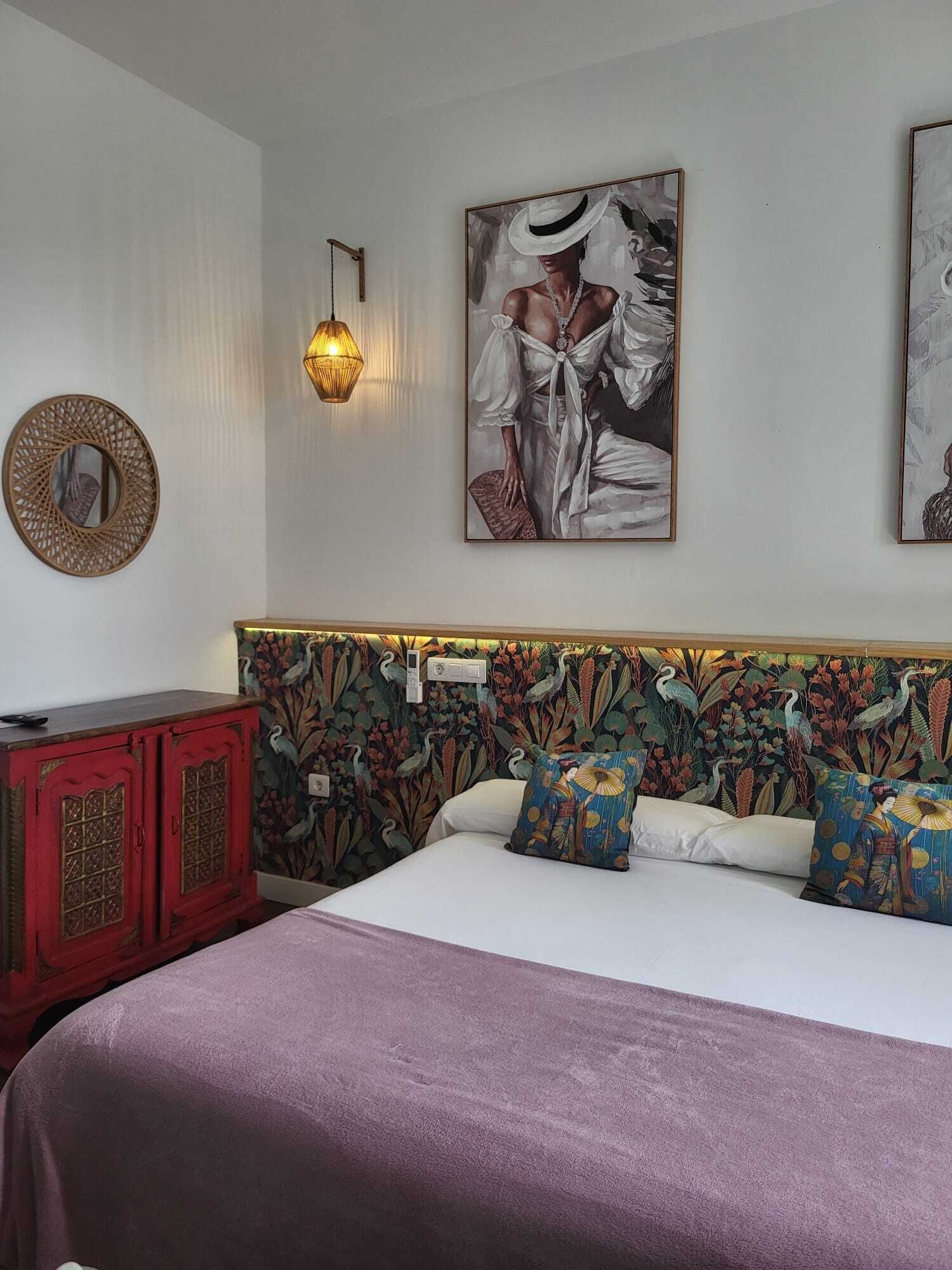 Een slaapkamer met een bed, een rode kast, een wandlamp en twee kunstwerken in lijsten.