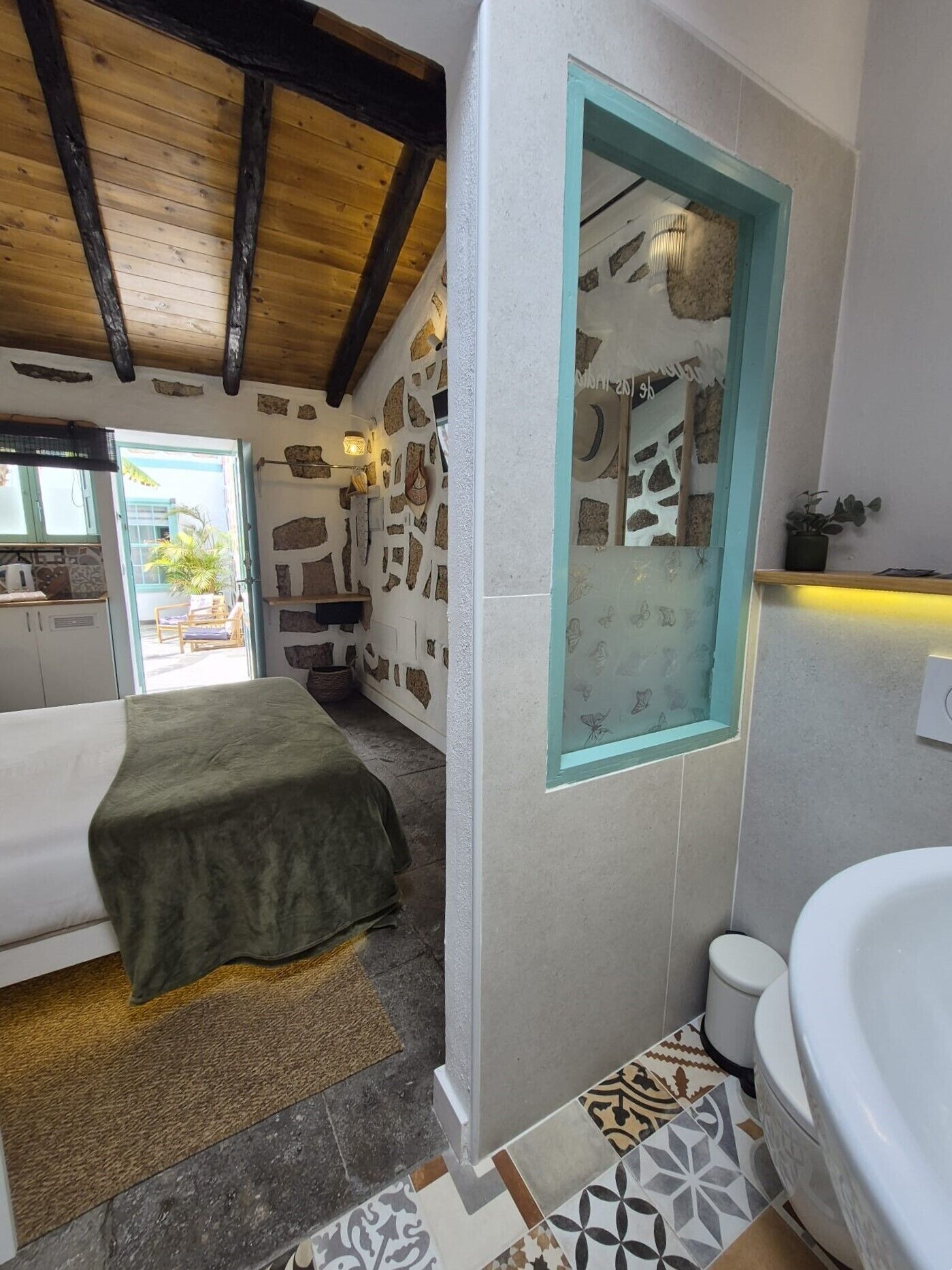 Una habitación con cama, una mesita, baño con bañera y pared de piedra.